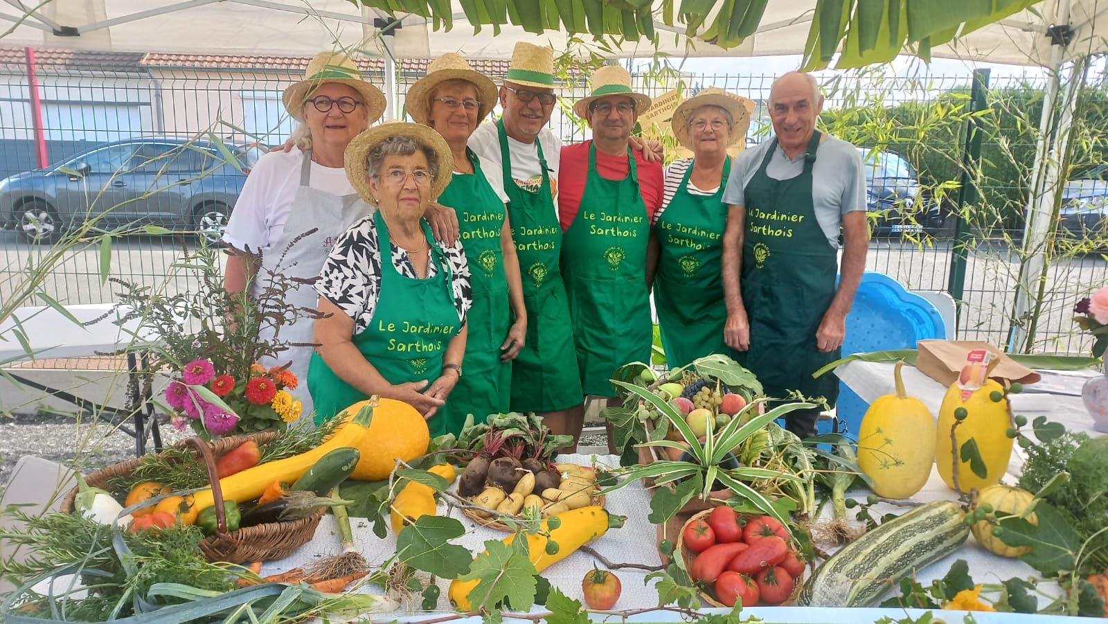Les membres du Jardinier Sarthois, tabliers verts et chapeaux de paille, devant leur stand de légumes et de fleurs